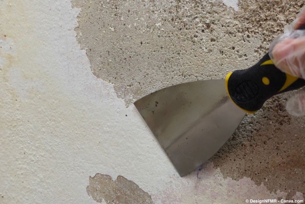 Abblätternde Farbe wird mit Spachtel von der Kellerwand entfernt