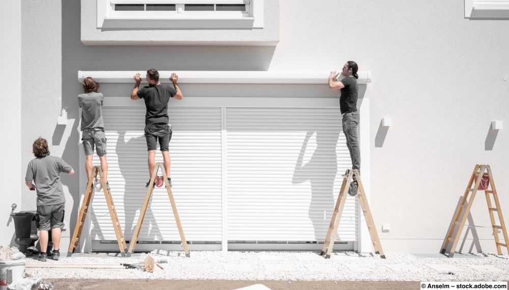 Mehrere Handwerker hängen eine Markise an Halterungen an der Hauswand ein