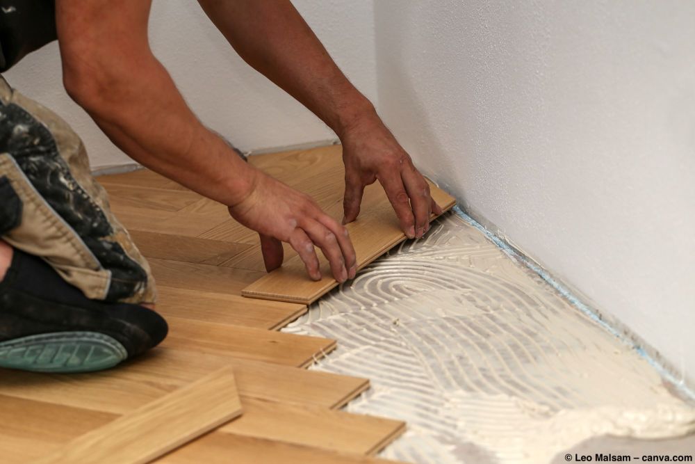 Person verlegt Fischgrät-Parkett in einem frischen Klebebett.