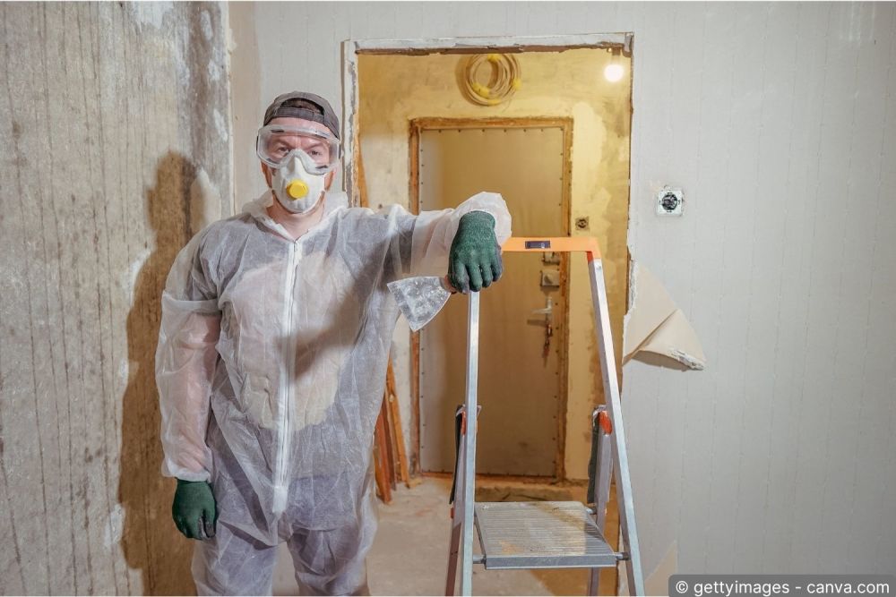 Handwerker mit Atemschutzmaske und Schutzanzug bei einer Sanierung