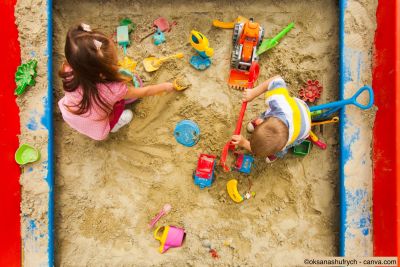 Zwei Kinder sitzen in einem Sandkasten im Garten und spielen mit bunten Förmchen und einer Schaufel