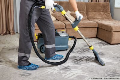 Reinigungskraft in Schutzkleidung reinigt Teppich sorgfältig mit leistungsstarken Staubsauger