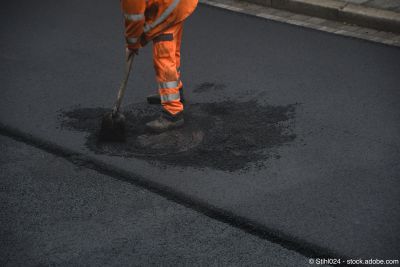 Strassenarbeiter arbeitet beim Asphaltieren mit Schaufel an Kanaldeckel