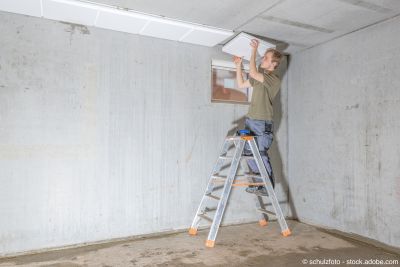 Handwerker auf Leiter dämmt Kellerdecke
