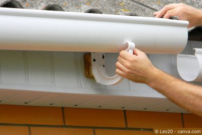 Detailansicht einer montierten Dachrinne mit befestigtem Fallrohr unter dem Dachvorsprung.