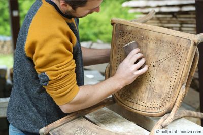 Handwerker schleift die Sitzfläche eines alten Holzstuhls mit Schleifpapier