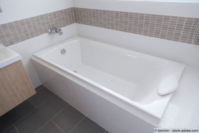Weisse eingebaute Badewanne mit Nackenstütze in einem modernen Badezimmer mit grauen Mosaikfliesen