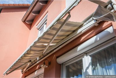 Beschädigte Sonnenstore mit gerissenem Storentuch an einer Hausfassade