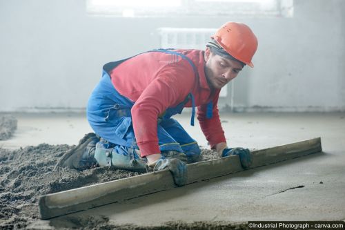 Bauarbeiter zieht Zementestrich auf einem Innenboden auf einer Baustelle glatt