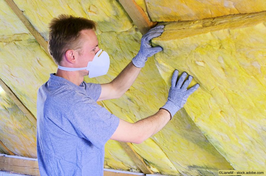 Handwerker mit Atemschutz daemmt einen Dachstock von innen