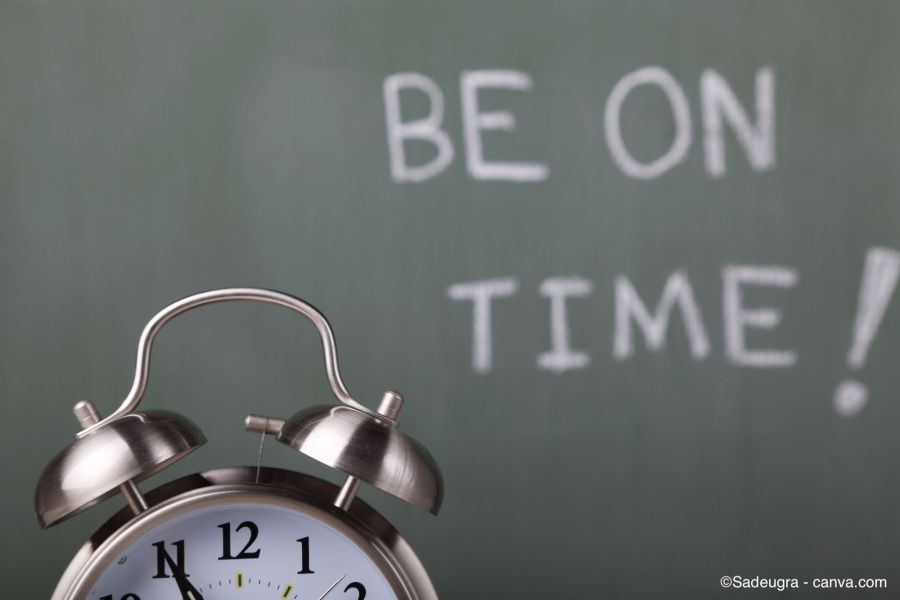 Wecker vor einer Tafel mit der Aufschrift «BE ON TIME!»