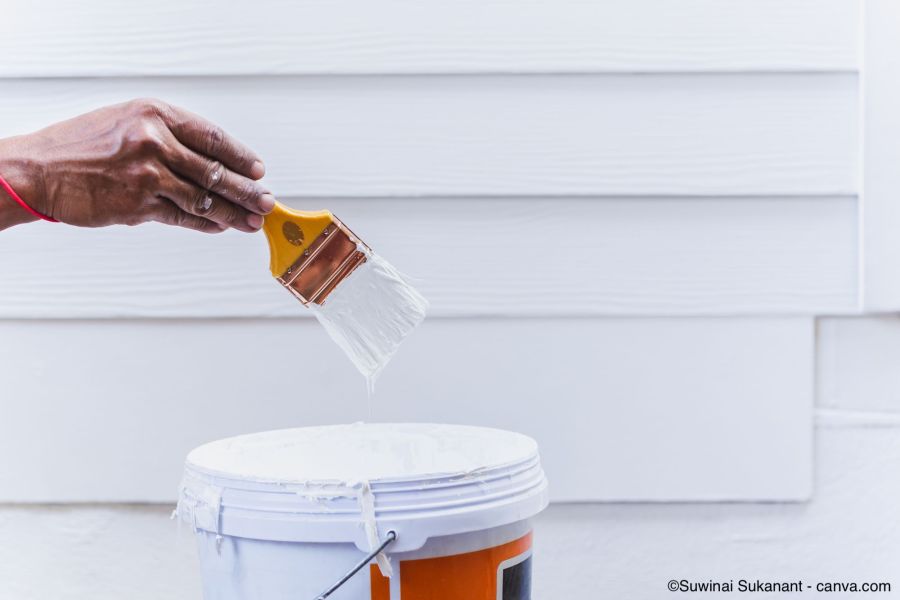 Mann bemalt eine Holzfassade mit weisser Farbe