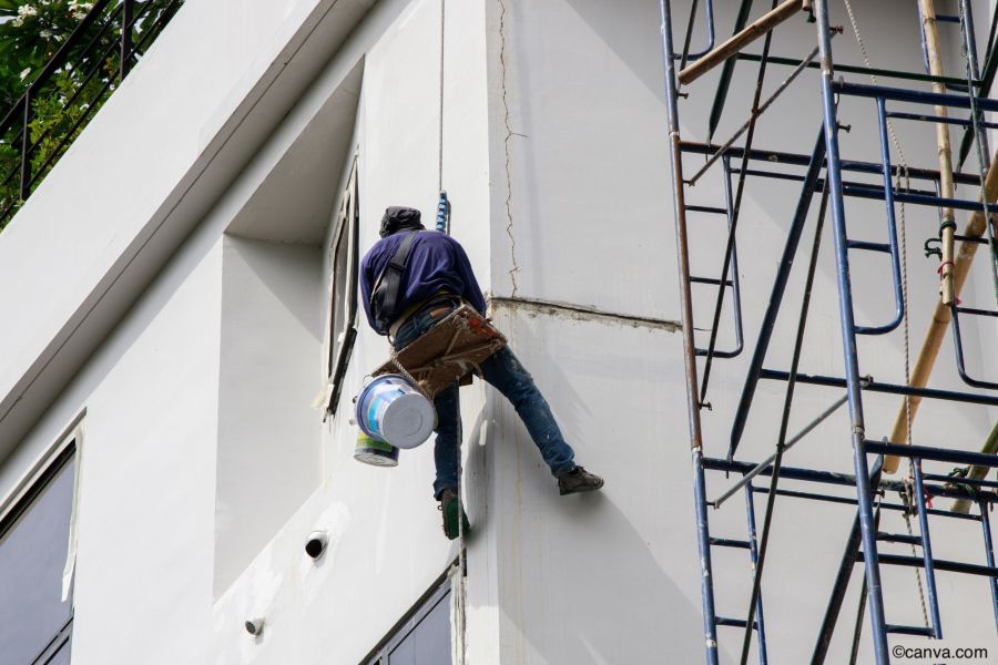 Handwerker, der an einem Seil hängt, um die Fassade eines Gebäudes zu streichen