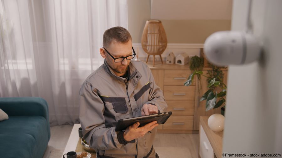 Männlicher Installateur richtet mit einem Tablet einen Bewegungsmelder in einer Wohnung ein