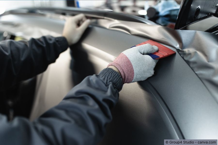 Hand mit Rakel glättet graue Autofolie auf einer Karosseriefläche