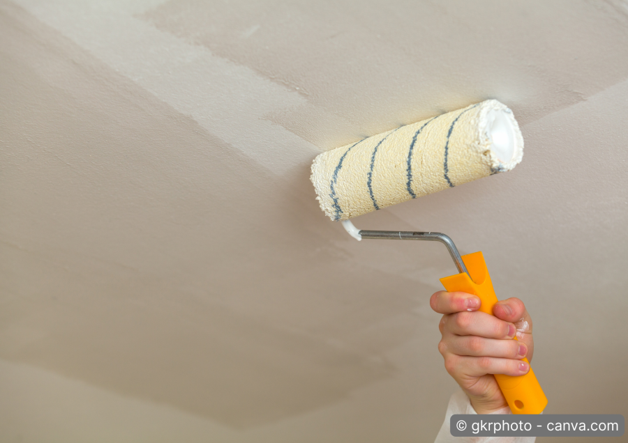 Maler streicht Decke mit Farbrolle