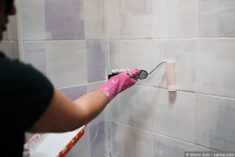 Mann streicht Badezimmerfliesen mit Farbrolle