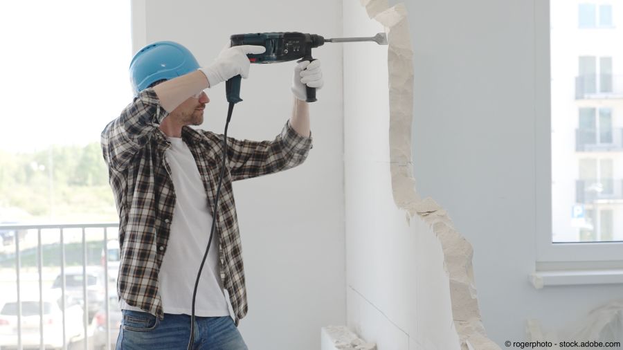 Ein Bauarbeiter in Schutzkleidung, der mit einem Bohrhammer eine Wand abreisst