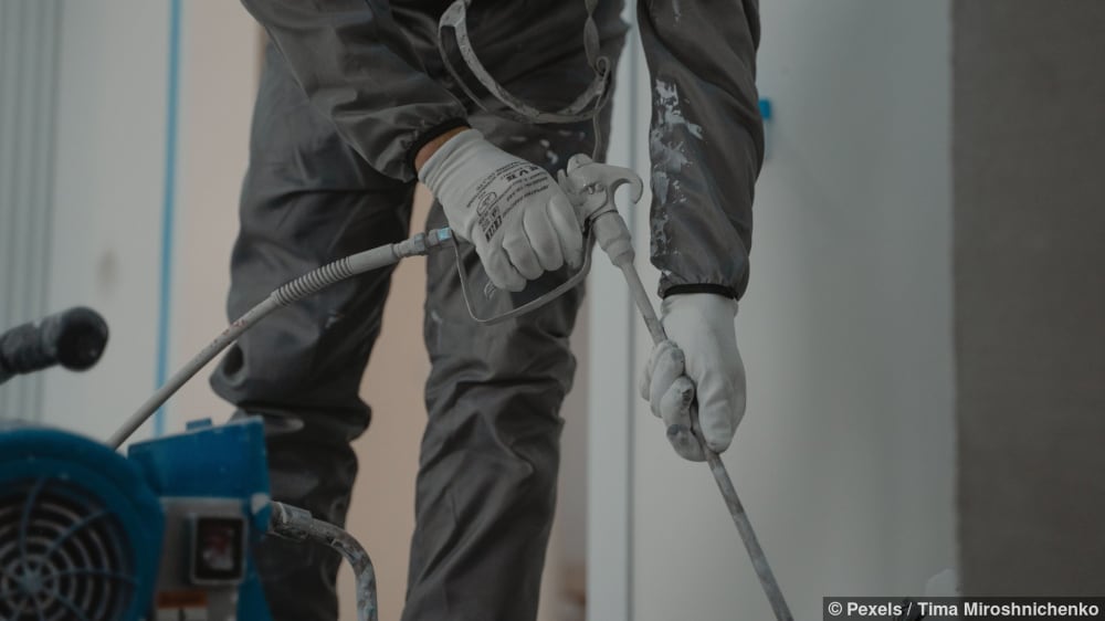 Arbeiter in Schutzkleidung benutzt Hochdruckreiniger, um Graffiti zu entfernen