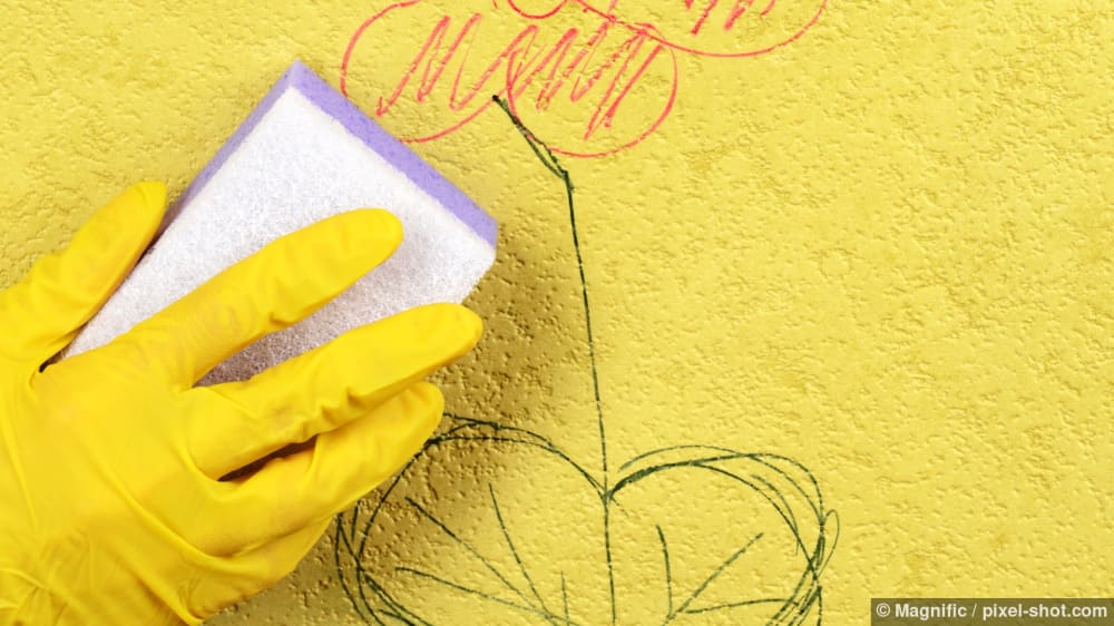 Eine behandschuhte Hand reinigt eine Wand