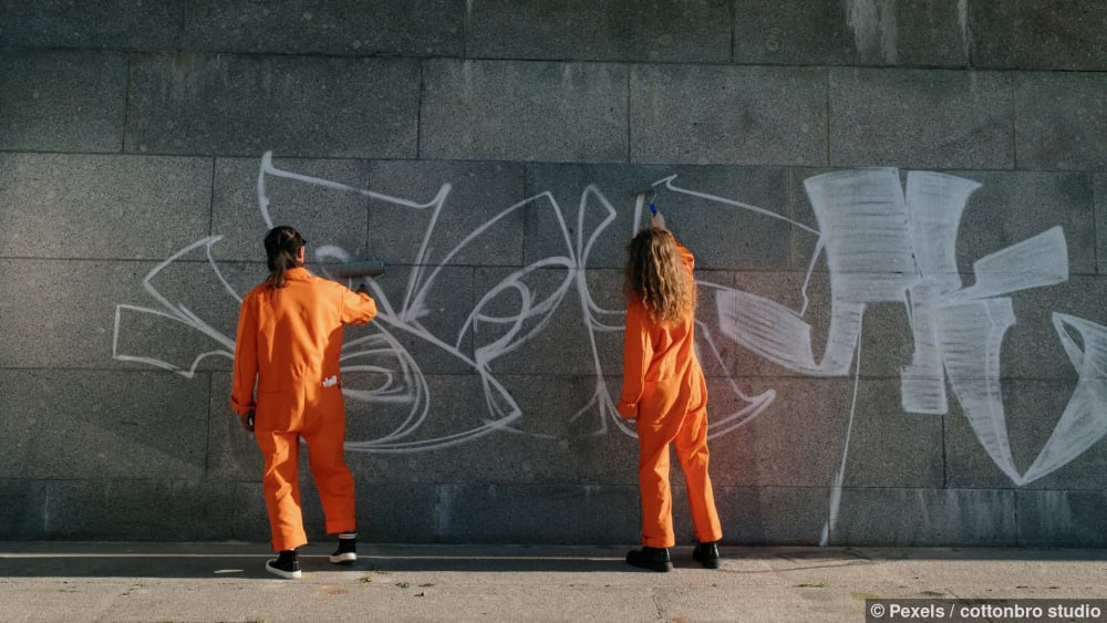 Zwei Facharbeiter in orangefarbenen Uniformen entfernen Graffiti von einer Betonwand