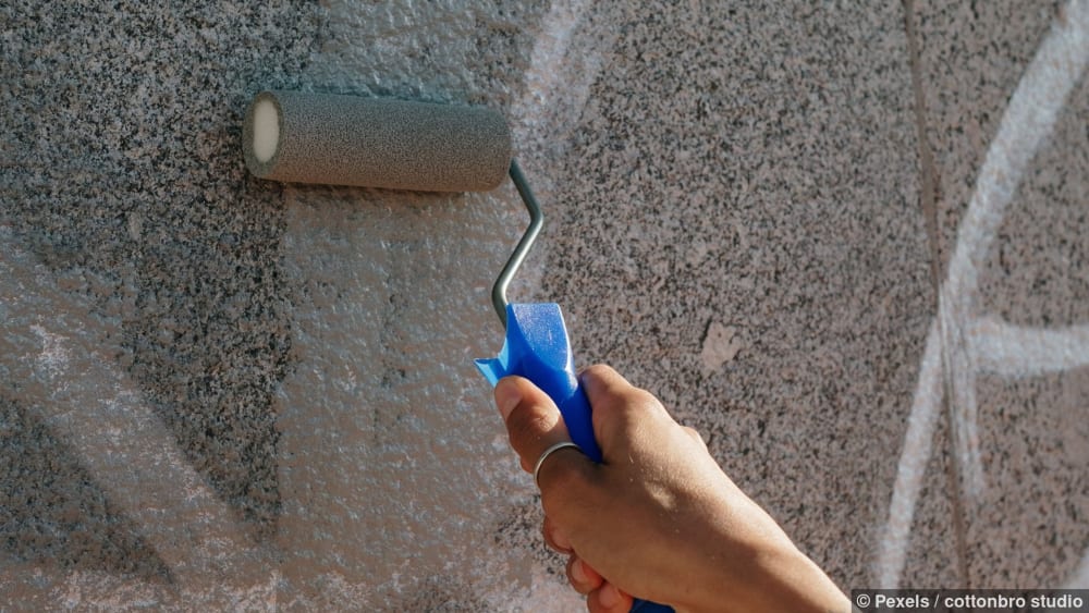 Nahaufnahme einer Hand, die Graffiti entfernt, indem sie es mit einer Farbrolle überdeckt