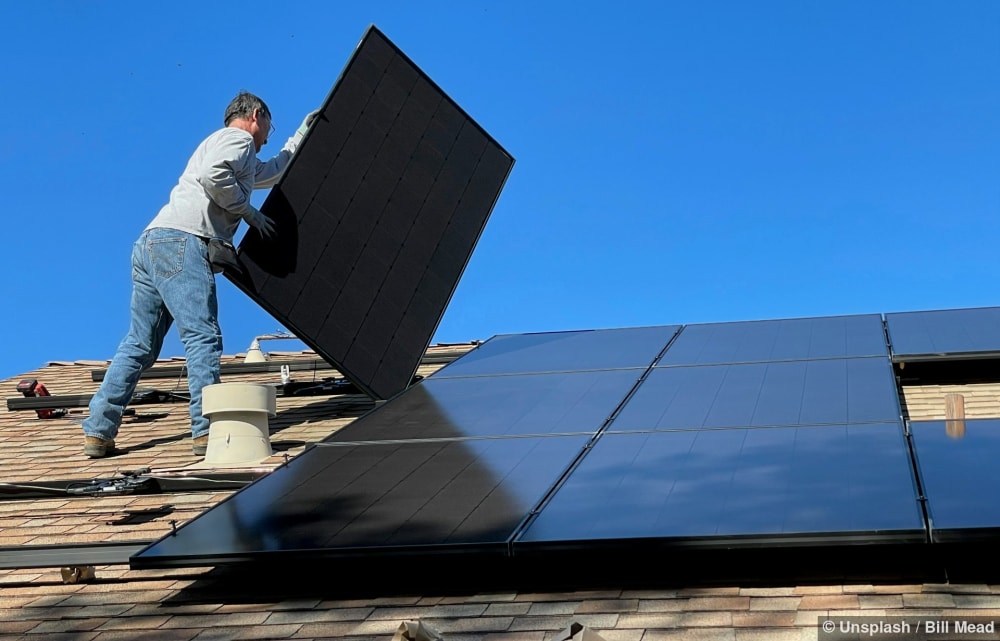 Eine Person installiert ein schwarzes Solarmodul auf einem Schrägdach