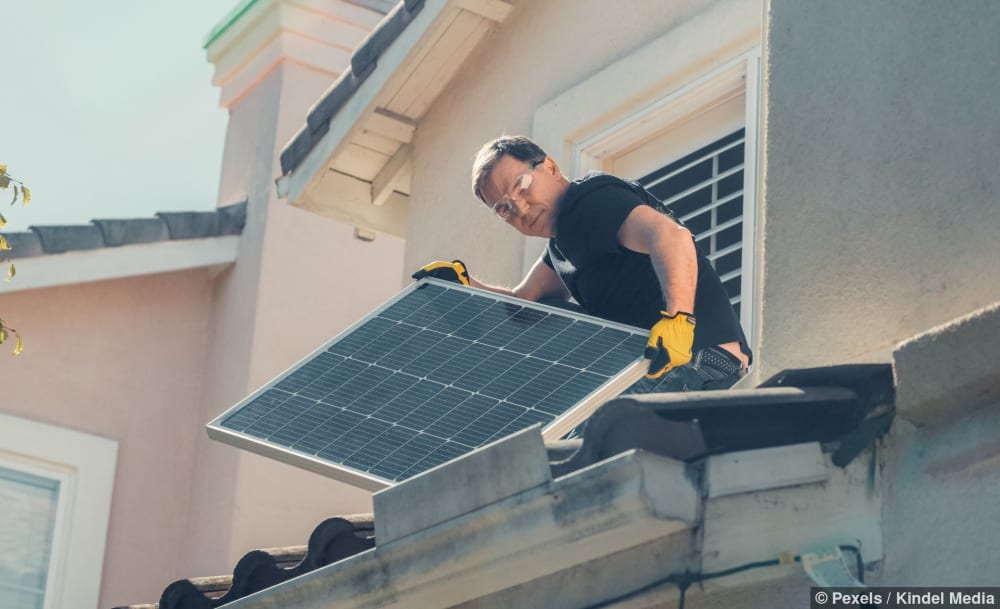 Techniker in Schutzkleidung installiert Solarpanels auf einem Hausdach