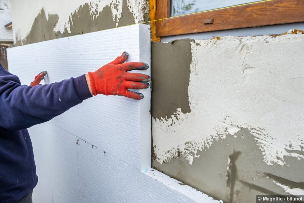 Bauarbeiter montiert Dämmplatten aus Styropor an einer Hausfassade