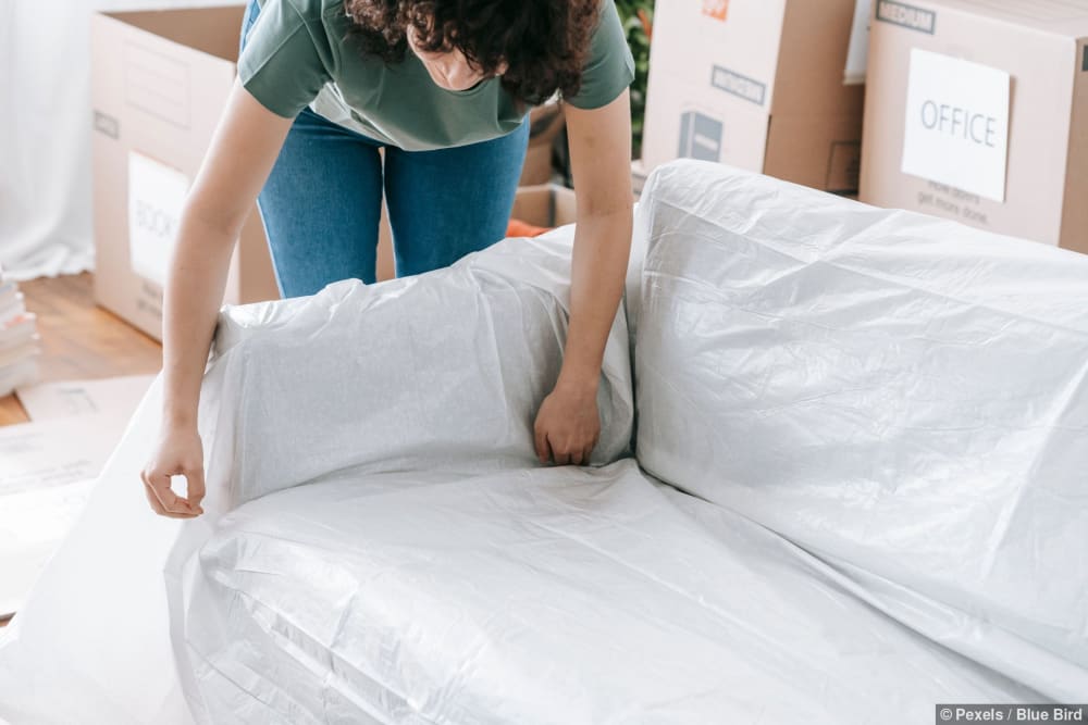 Eine Frau wickelt vorsichtig ein Sofa in schützendes Material, während sie Kisten packt
