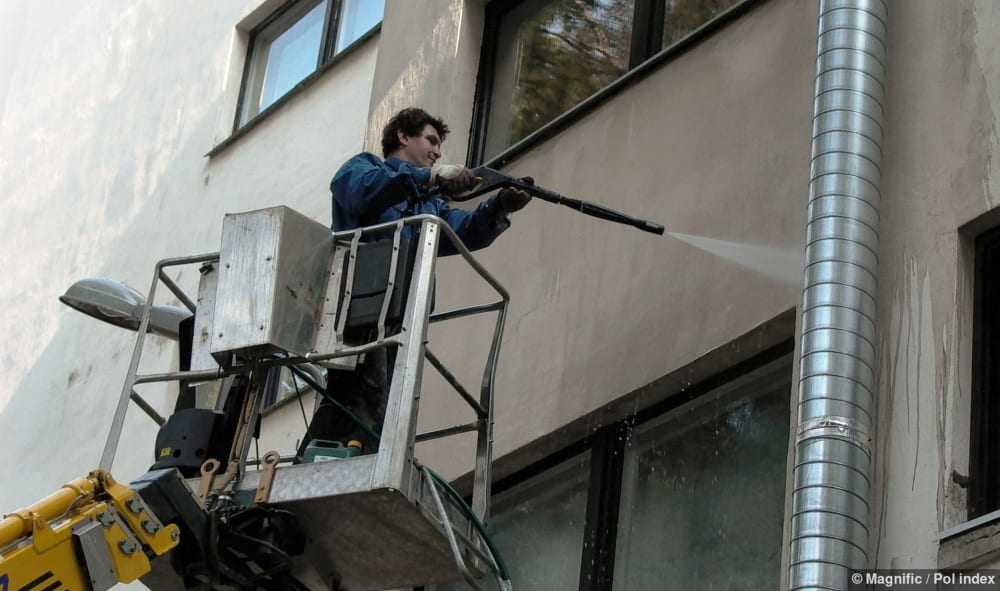 Arbeiter auf Hebebühne reinigt Putz an einer Fassade