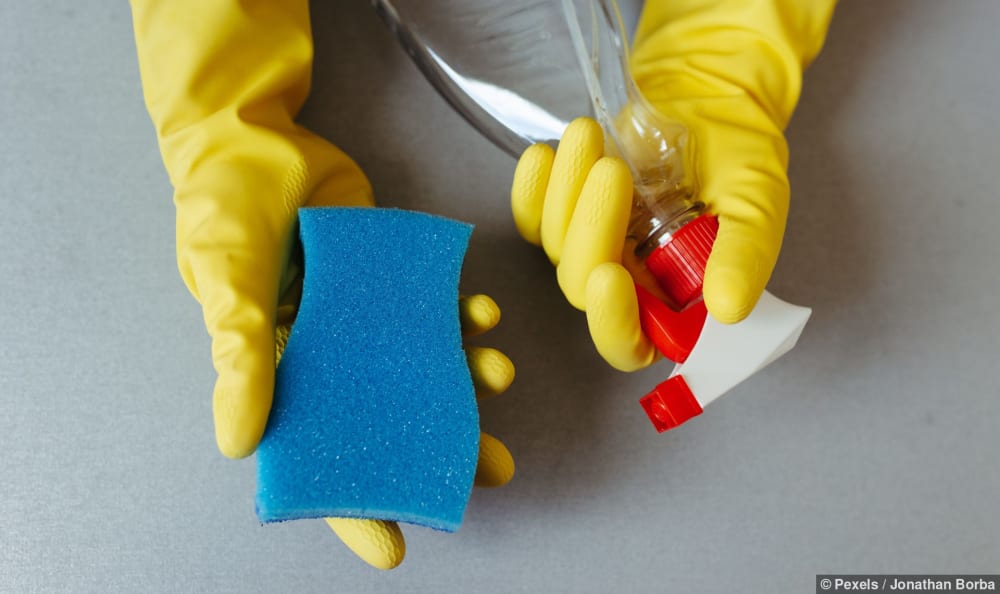 Hände mit gelben Handschuhen halten einen Schwamm und eine Sprühflasche für die Endreinigung