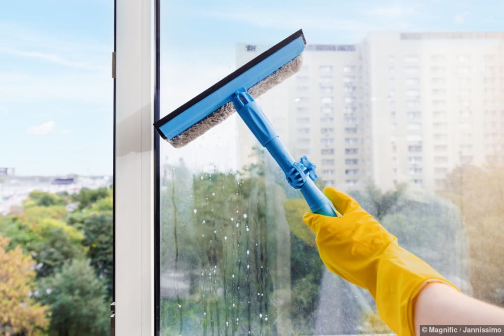 Hand in gelbem Handschuh reinigt bei Endreinigung ein Fenster mit einem Abzieher