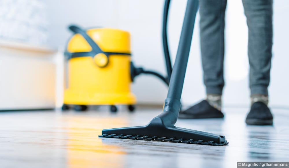 Eine Person saugt mit einem gelben Staubsauger den Boden in einem Zuhause