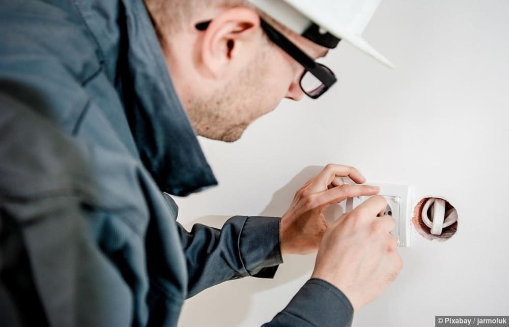 Ein Elektriker mit Schraubendreher arbeitet an Steckdose und führt Elektrokontrolle durch