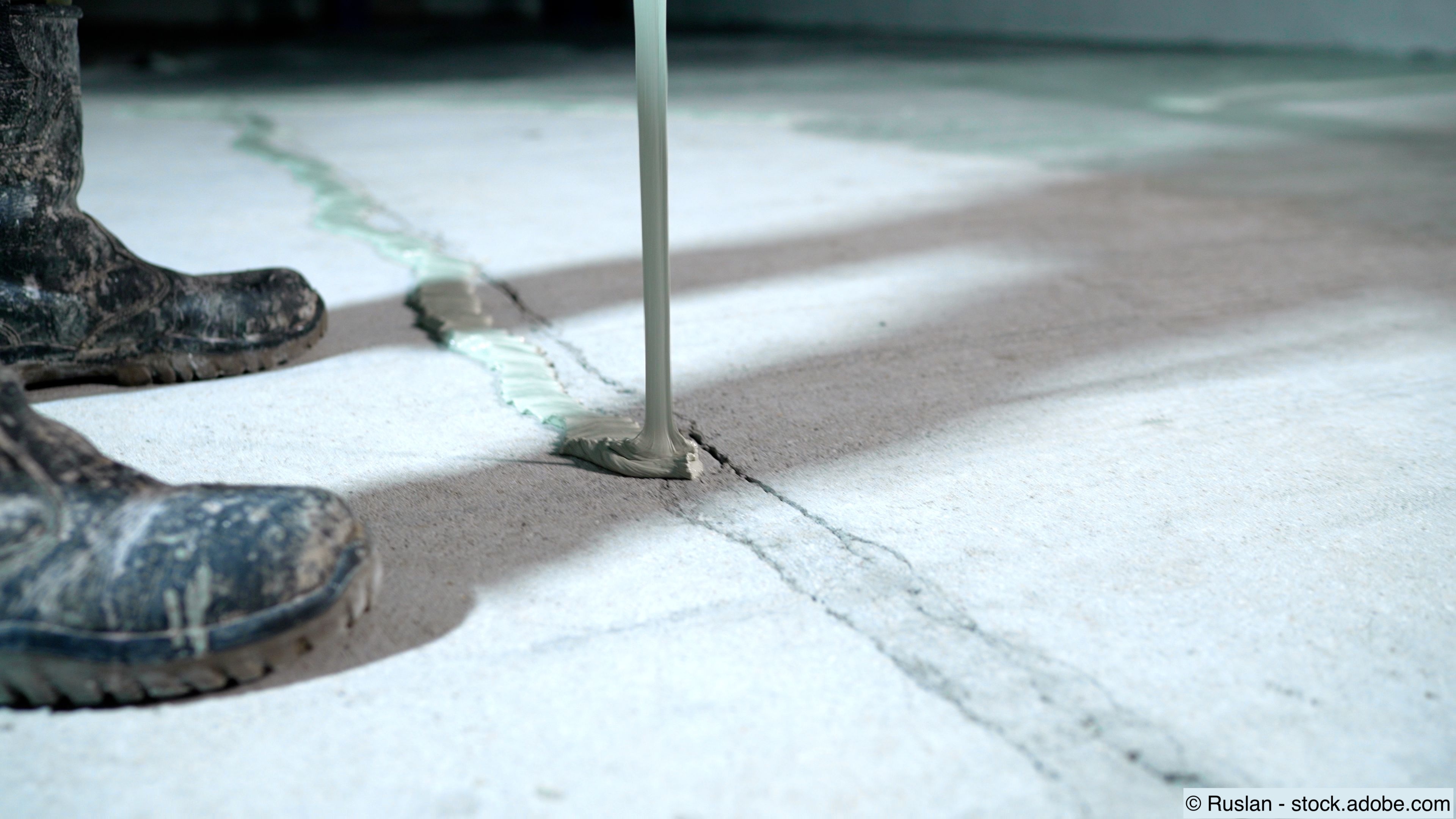 Handwerker beim Auftragen von Dichtungsmasse auf einen Riss im Betonboden